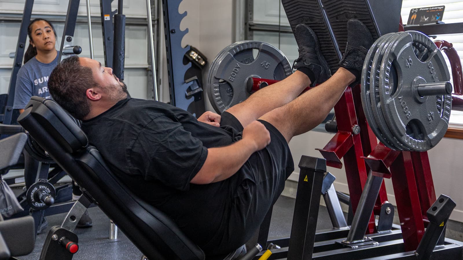 Lissa guiding a member through a leg-press set, hands-on.